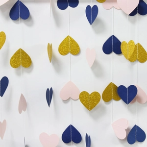 Close-up of glitter gold, navy, and pink paper heart garland on a white wall
