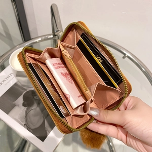 Brown zip-around short wallet with pink interior and plush ball charm in hand
