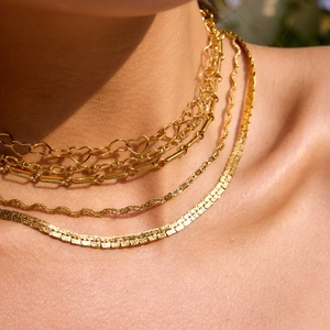 Nahaufnahme von mehrlagigen goldenen Schlangenketten am Hals für einen minimalistischen Look