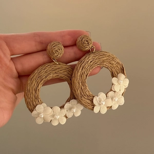 Detail of woven rattan hoop earrings with white fabric flowers and pearl accents