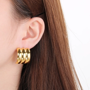 Detail of model wearing three-layered chunky golden C-shaped hoop earrings in 18k gold finish