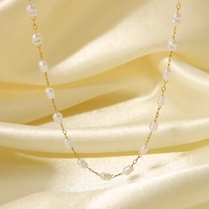 Macro shot of 18K gold plated necklace with small pearls on elegant golden silk fabric