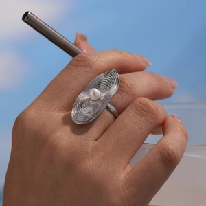 Minimalist silver ripple texture ring with white pearl detail on model against sky