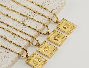 Détail de quatre pendentifs carrés en or 18K avec motifs arc-en-ciel et couronne gravés