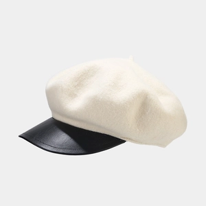Detailed shot of newsboy cap featuring white wool blend fabric and black leather visor
