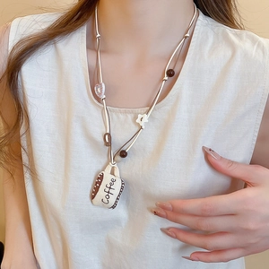 Detail showing hand-stitched fabric coffee cup pendant on a beaded necklace worn by model