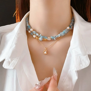 Macro detail of a double-layer necklace with blue sea stones and a golden pearl pendant