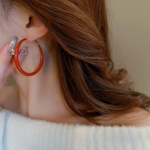 Close-up of a large glossy red hoop earring worn by a model in a minimalist style