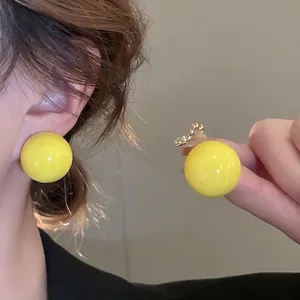 Minimalist bright yellow spherical stud earrings with glossy finish on model