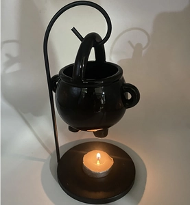 Detailed view of a black ceramic cauldron oil burner with metal stand and lit tea light