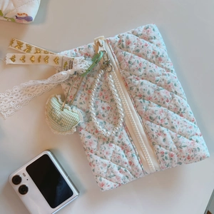 Quilted floral makeup bag with pearl handle and heart charm next to a phone