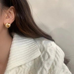 Close-up of elegant gold and cream knot stud earrings worn by a model in a knit sweater