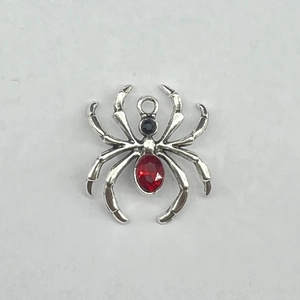 Detailed view of silver spider charm with red faceted gemstone and black crystal accent