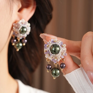Detail of vintage flower earrings with purple petals and hanging pearls on a model