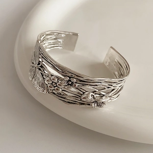 Macro view of vintage silver hollow bangle featuring brushed butterfly and flower patterns