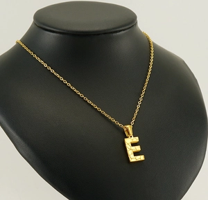 Close-up of hammered gold letter E pendant on an O-chain worn on a black model bust
