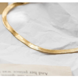 Macro shot of a flat gold snake bone necklace resting on elegant paper texture