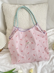 Pink checkered tote bag with red bow print and purple wavy trim on a white bed