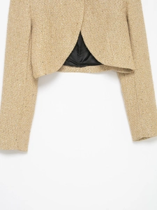 Detail of gold tweed jacket with sequins featuring a V-shaped slit and textured knit fabric