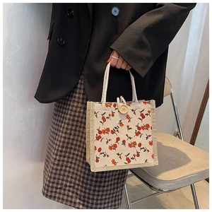 Detail of a vintage floral handbag with cream canvas and white rope handles held by a model