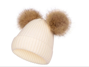 Détail du bonnet en tricot blanc avec deux pompons en fausse fourrure marron sur le dessus