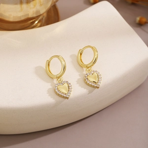 Close-up of golden heart earrings with sparkling rhinestones on a minimalist display