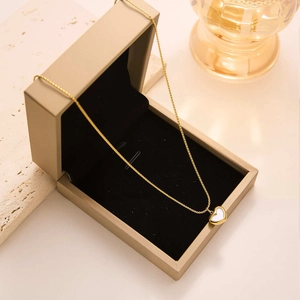 Close-up of golden heart pendant with white mother-of-pearl inlay in a beige jewelry box