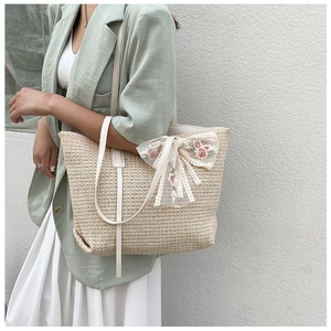 Close-up of beige woven tote bag featuring floral lace embroidery and ribbon detail