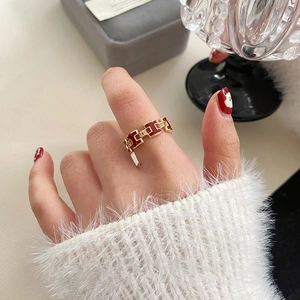Detail of gold-plated H-shaped ring with red enamel and pavé zircons on finger