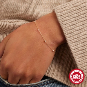 Pulsera de plata S925 dorada con perlas lucida por modelo sobre un suéter de punto