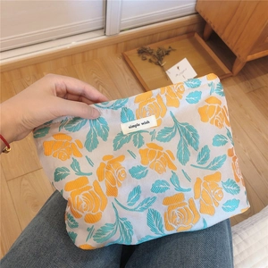 Detail of floral tapestry makeup bag with orange rose embroidery and brand label