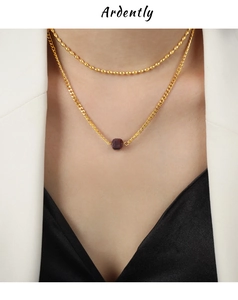 Detail of layered gold beaded chain and necklace with a deep red square gemstone pendant