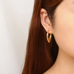 Close-up of golden C-shaped hoop earrings with hammered texture on a model