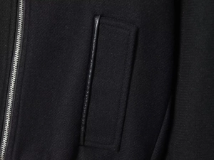 Detailed macro view of black wool coat featuring silver metal zipper and faux leather pocket trim