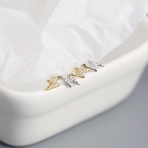 Macro shot of silver and gold lightning bolt stud earrings with sparkling zircon details