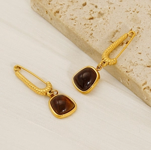 Detail of 18K gold-plated safety pin earrings with square amber stone on beige stone