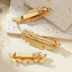 Three-piece gold metal feather and leaf hair clips on textured stone display