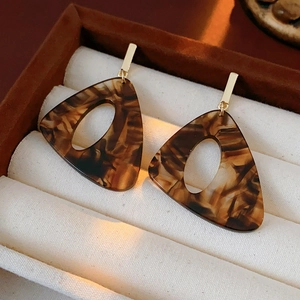 Macro shot of triangle leopard resin earrings with gold pins in a velvet jewelry box