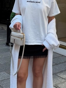 Detail of summer satin mini skirt with delicate black lace trim and white knit cardigan