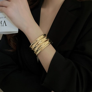 Detail of wide gold wave-textured cuff bracelet worn over a stylish black suit sleeve
