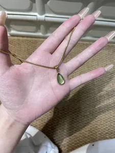 Macro view of gold chain holding a translucent green water drop pendant for women