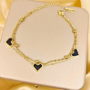 Double-layered gold titanium steel bracelet with black heart charms on silk background