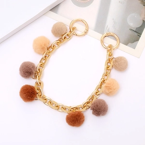 Detailed view of a golden metal chain with brown and beige faux rabbit fur pompom charms