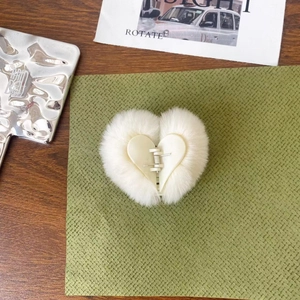 Detailed top view of a white heart-shaped plush hair claw clip on an olive green backdrop