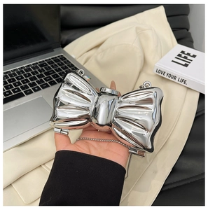Detail of silver bow-shaped metal clutch with fine chain strap held in hand