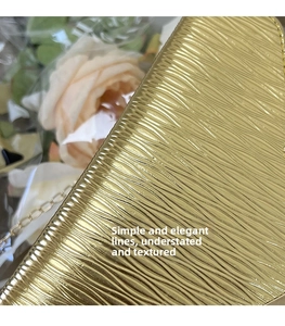 Détail macro de la texture cuir doré ondulé et de la fine chaîne dorée du sac à main