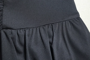 Detail of black A-line dress showing pleated fabric texture and high-quality stitching