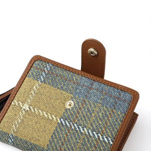 Detail of plaid tweed wallet with brown leather trim and golden metal snap fastener