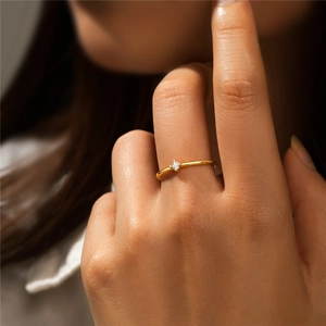 Close-up of minimalist 18K gold ring with a sparkling round zircon stone on finger