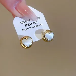 S925 silver heart stud earrings with white inlay and golden finish held by hand